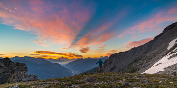 istock Man standing on mountain top raising arms, sunrise light colorful sky scenis landscape, conquering success leader concept. 1001625310