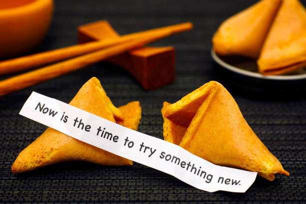 Paper strip with phrase Now is the Time to Try Something New from fortune cookie, another cookie and chopsticks on black napkin background.