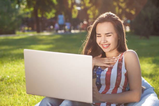 bela jovem sentada no laptop de uso de saco de feijão, enquanto descansava na grama no parque do sol - coffee bean bag human hand - fotografias e filmes do acervo