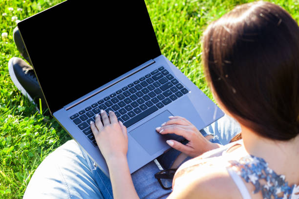 istock Close up hands on keyboard. Woman working on laptop pc computer with blank black empty screen to copy space in park on green grass sunshine lawn outdoors 1001653706