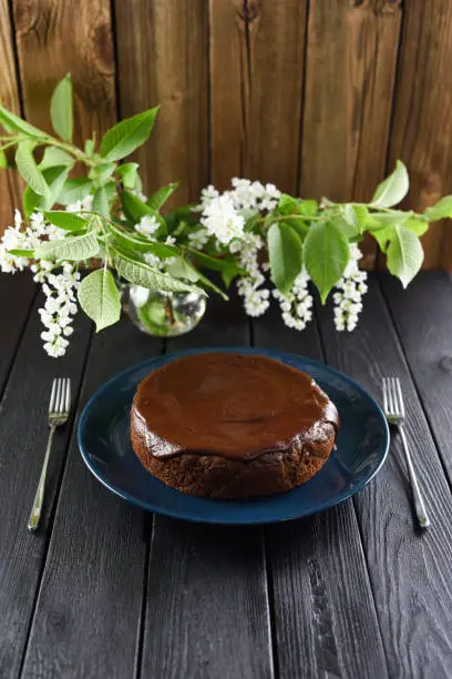 Delicious homemade dessert. Bird cherry cake with chocolate icing decorated with bird cherry flowers on navy blue plate on black background vertical