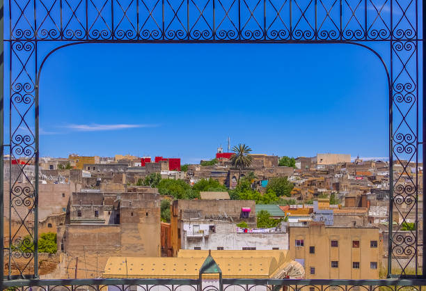 View of ancient rooftops of the Fez medina through an ornate metal window frame View over the ancient yellow clay rooftops of the Fes medina through an ornate metal window frame marrakesh riad stock pictures, royalty-free photos & images