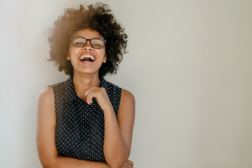 Portrait of excited young woman standing by a wall and laughing. Cheerful young african female with curly hair and spectacles.