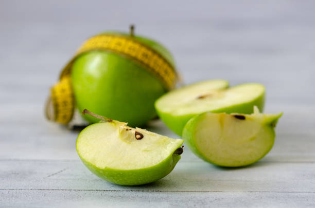 istock Dieting concept.Whole and sliced green apples with measuring tape 1001734304