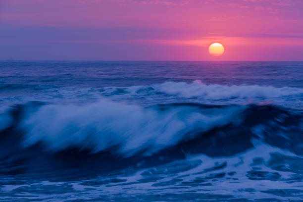 Dramatic pinkish sunrise over Manasquan beach in New Jersey featuring big wave on the foreground and sun on the background