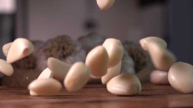 Garlic falling to wood cutting board, on kitchen background. Slow motion 240 fps. Sony rx 10