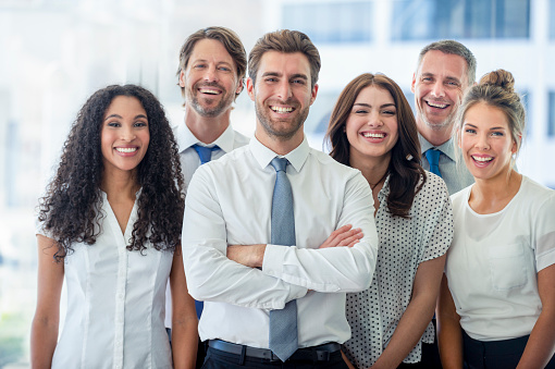 Portrait of handsome smiling businessman with his colleagues. Multi-ethnic group of business persons standing in modern office. Successful team leader and his team in background.