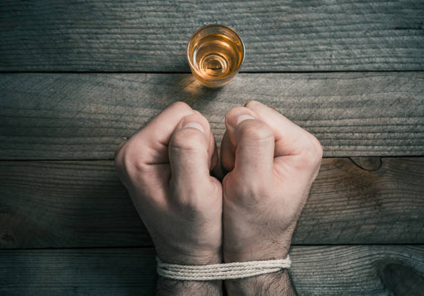 Quit Drinking Alcohol Concept With A Booze Glass In Front Of 2 Tied Stressed Looking Clenched Fists stock photo