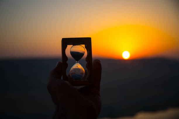 istock Life time passing concept. Hand holding hourglass with sunset sky background. 1001811696
