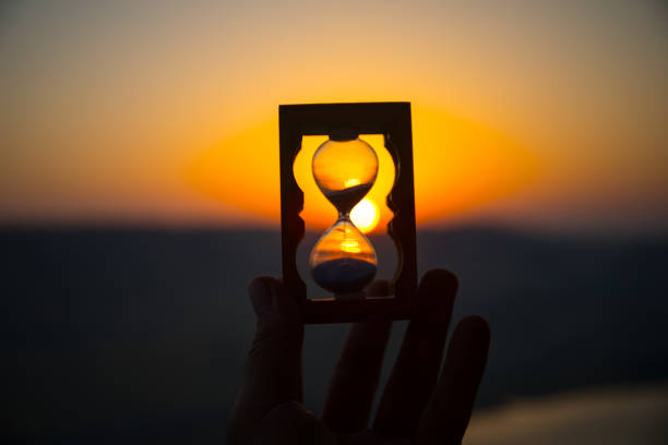 istock Life time passing concept. Hand holding hourglass with sunset sky background. 1001811698