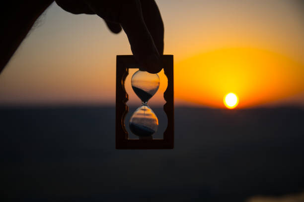 istock Life time passing concept. Hand holding hourglass with sunset sky background. 1001811702