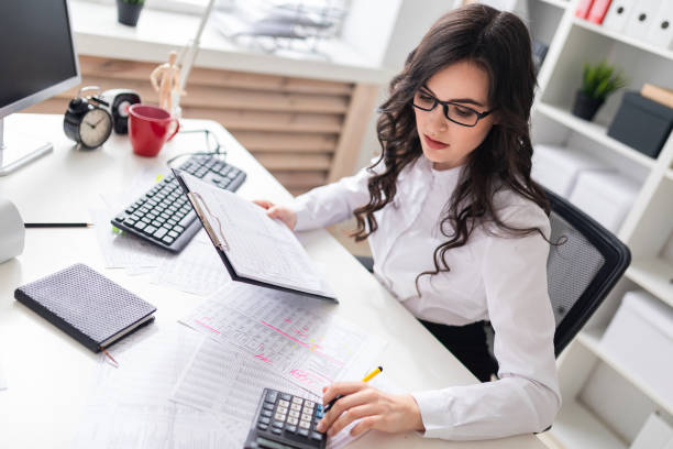 a young girl is sitting at the office desk and is blessing on the calculator. - occupation office bill finance imagens e fotografias de stock