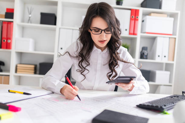 istock A young girl is sitting at the office desk, working with a calculator and documents. 1001814088