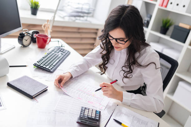 istock Young girl sits at office desk and fills documents with her left hand. 1001814096