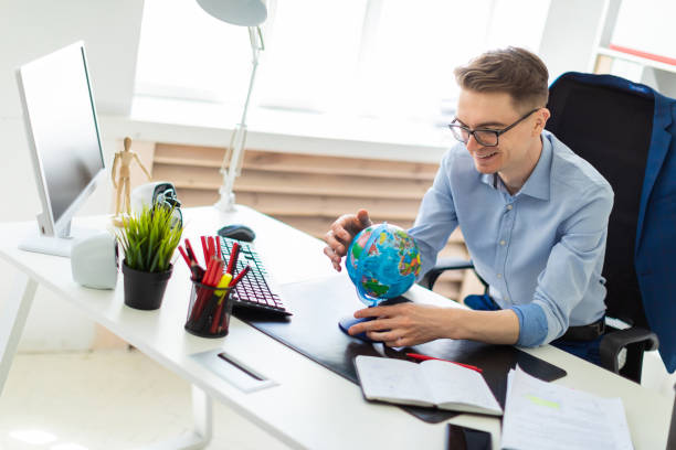 istock A young man sits in the office at a computer desk and holds a globe in his hands. 1001814250