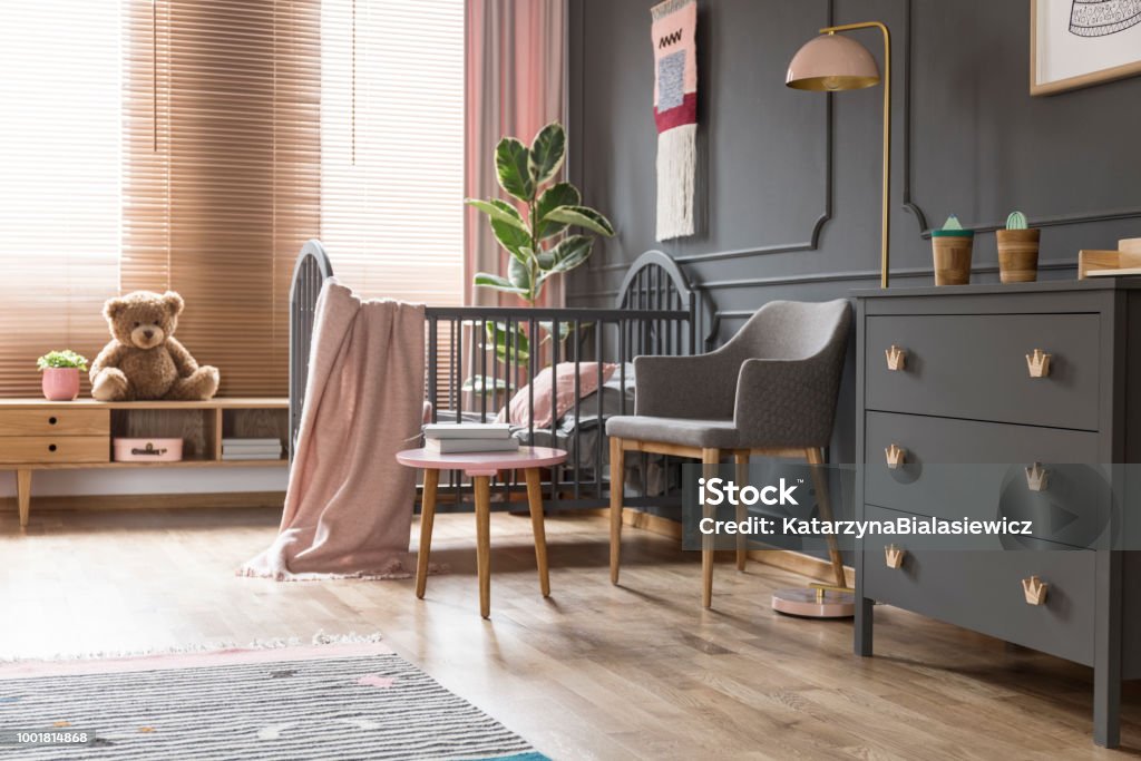 Real photo of a cot standing next to an armchair, lamp and cupboard in dark and classic baby room interior Bedroom Stock Photo