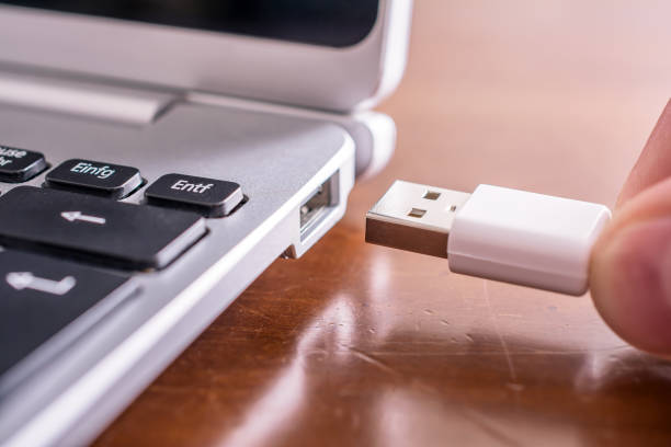 Male Hand Connecting A White USB Cable To The USB Port Of A Small Notebook stock photo