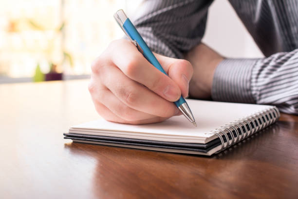 Front View Of A Man In Business Shirt Writing In A Blank Notepad With A Biro stock photo