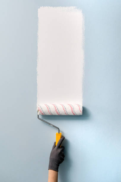 A hand with a roller paints the wall with white paint stock photo