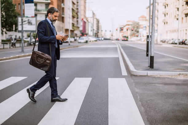 Businessman On Zebra Crossing Mature Businessman Crossing The Street And Using Phone crossing stock pictures, royalty-free photos & images