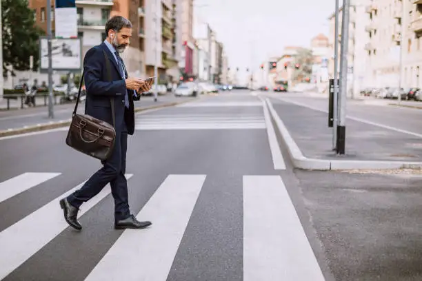 Mature Businessman Crossing The Street And Using Phone