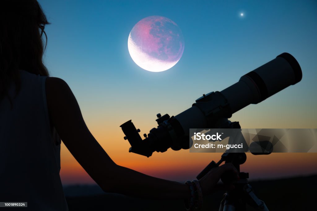 Girl looking at lunar eclipse through a telescope. My astronomy work. Lunar Eclipse Stock Photo