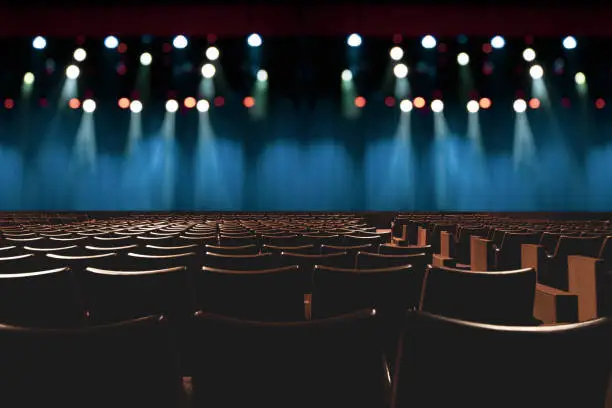 Photo of empty vintage seat in auditorium or theater with lights on stage.