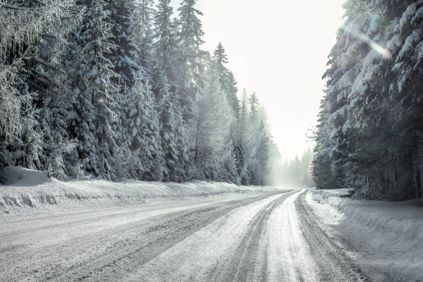istock View from a car riding through snow covered winter road curve, lit by strong sun backlight and fog and haze in distance - dangerous driving conditions. 1001943836