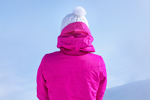 Detail view from back to young woman in pink ski jacket standing on top of the mountain.
