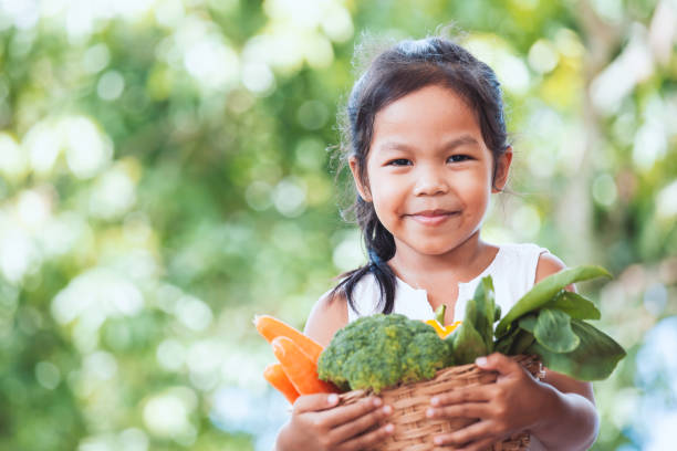 Cute asian child girl holding basket of vegetables prepare for cooking with her parent stock photo