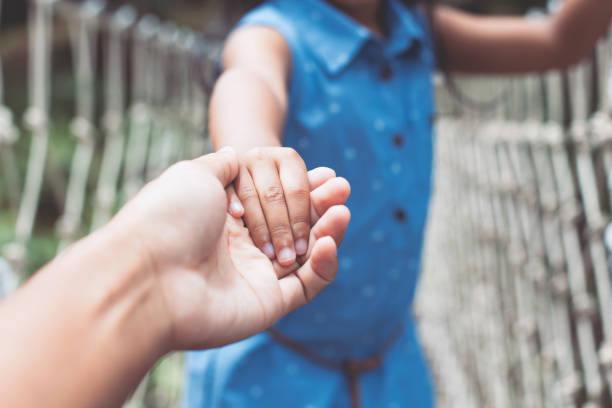 Parent and child holding hand together while walking on the hanging rope bridge across the river Parent and child holding hand together while walking on the hanging rope bridge across the river in the forest with love and care bridge hand stock pictures, royalty-free photos & images