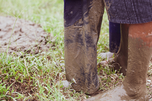 Dirty Wornout Construction boots on green grass and construction worker in the background. Copy space