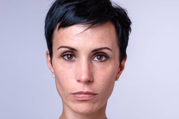 Attractive woman with a short modern hairstyle and big brown eyes looking solemnly at the camera, head shot over grey