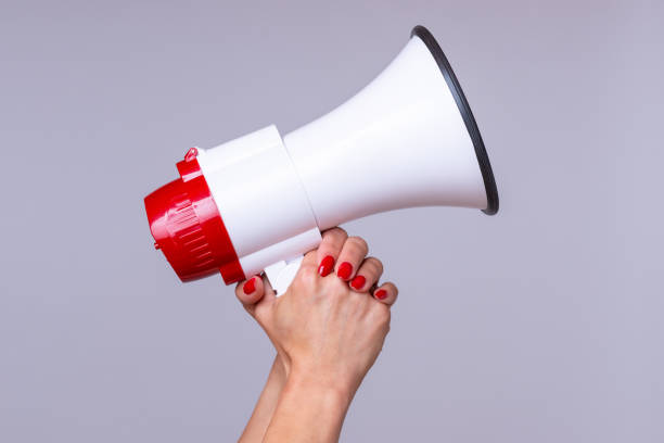 Woman holding up a loud hailer or megaphone Woman holding up a loud hailer, bullhorn or megaphone as she prepares to stage a protest or demonstration to air her grievances horned stock pictures, royalty-free photos & images