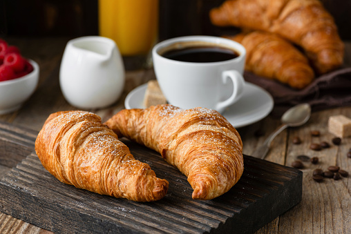 Breakfast with croissants, coffee, orange juice and berries on wooden table. Closeup view, selective focus