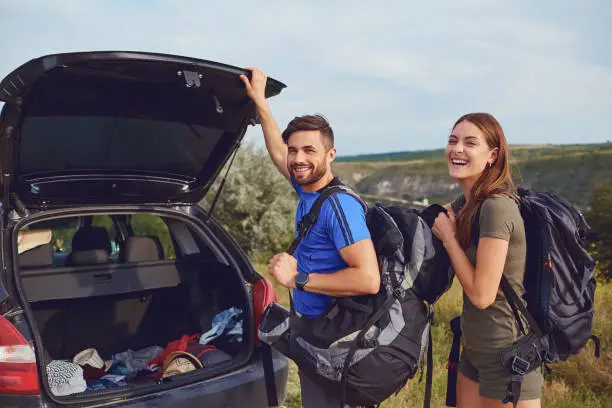 Photo of A couple of tourists with backpacks near a car on  natur