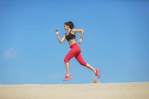 Young female runner mid air during a run on a sand dune