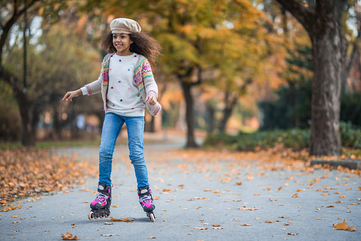 Full length of carefree black girl having fun while roller skating in autumn.