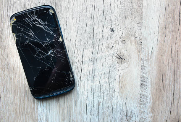 istock Crashed black smartphone is lying on the wooden background. Broken lcd touch screen. Information technology photo. 1002003970