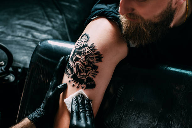 ritagliato scatto di tatuatore in guanti lavorando sul tatuaggio sulla spalla in salone - tatuare foto e immagini stock