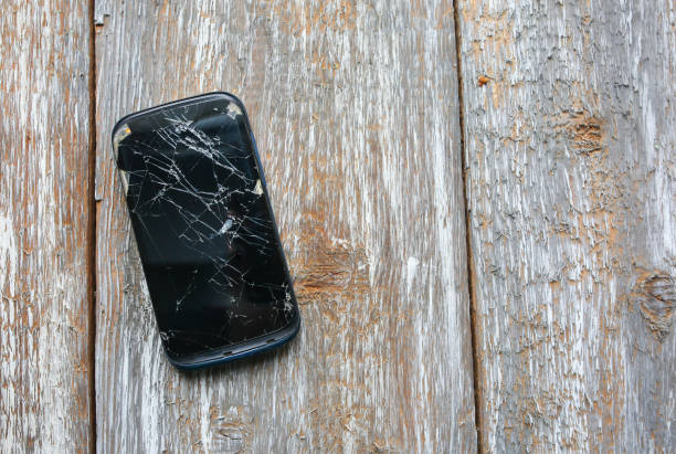 istock Crashed black smartphone is lying on the wooden background. Broken lcd touch screen. Information technology photo. 1002010436