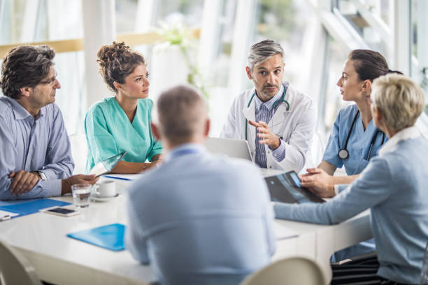 Team of doctors and business people talking on a meeting at doctor's office. Male doctor and his female colleagues talking to team of business people on a meeting in the hospital. surgeon photos stock pictures, royalty-free photos & images