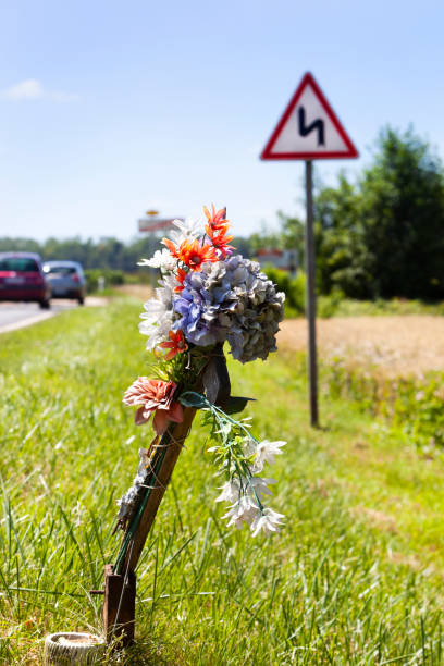 carretera conmemorativa junto a una señal de curva peligrosa - memorial roadside cross cross shape fotografías e imágenes de stock