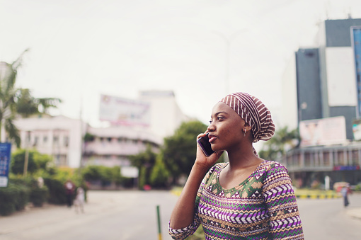 A beautiful young African business woman dressed in traditional authentic East African dress and headscarf talking on her mobile phone in the city centre of Dar es Salaam East Africa