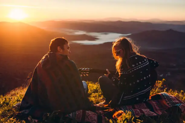 Young people meet the sunrise on the top of the mountain playing the guitar