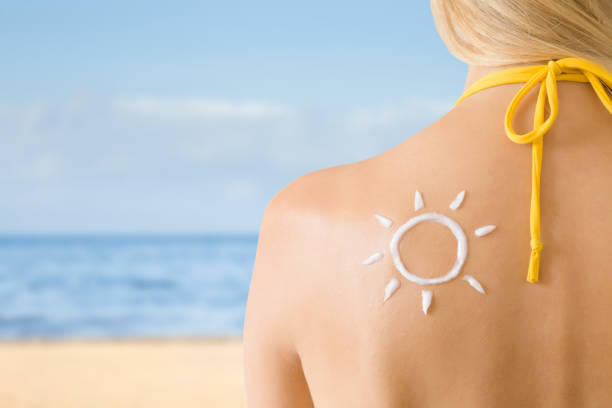 istock Sun shape created from sunscreen lotion on young woman's back. Skin protection. Hot day. Safety sunbathing concept. Copy space. Empty place for text on beach background. 1002041904