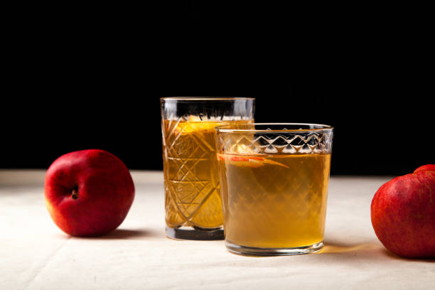 istock Two vintage glasses with apple cider on black background. Christmas beverages concept. Two red apples and rosemary sprig aside.  Warm backlight. Horizontal composition. Side view. 1002046812