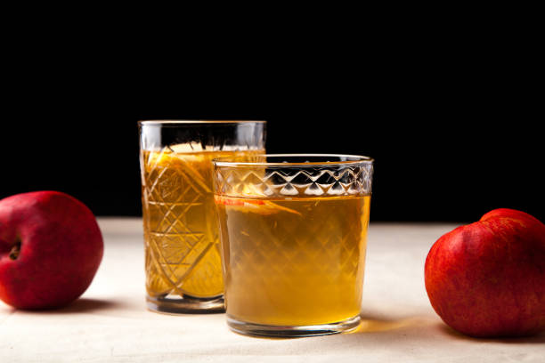 istock Two vintage glasses with apple cider on black background. Christmas beverages concept. Two red apples and rosemary sprig aside.  Warm backlight. Horizontal composition. Side view. 1002046826