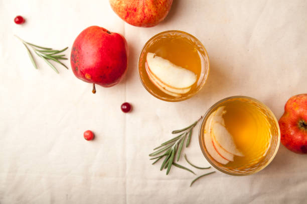 istock Two vintage glasses with apple cider on black background. Christmas beverages concept. Two red apples and rosemary sprig aside.  Warm backlight. Top view. 1002046976