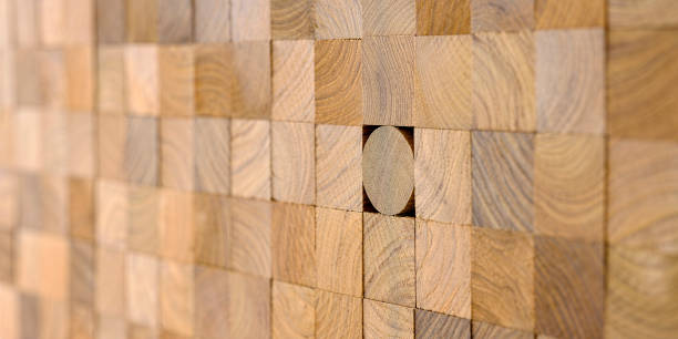 Many wood square block length profiles stacked up at the same length with one round profile length within the background standing out from the crowd. Concept image of individuality, going against the grain, standing out from the crowd etc.